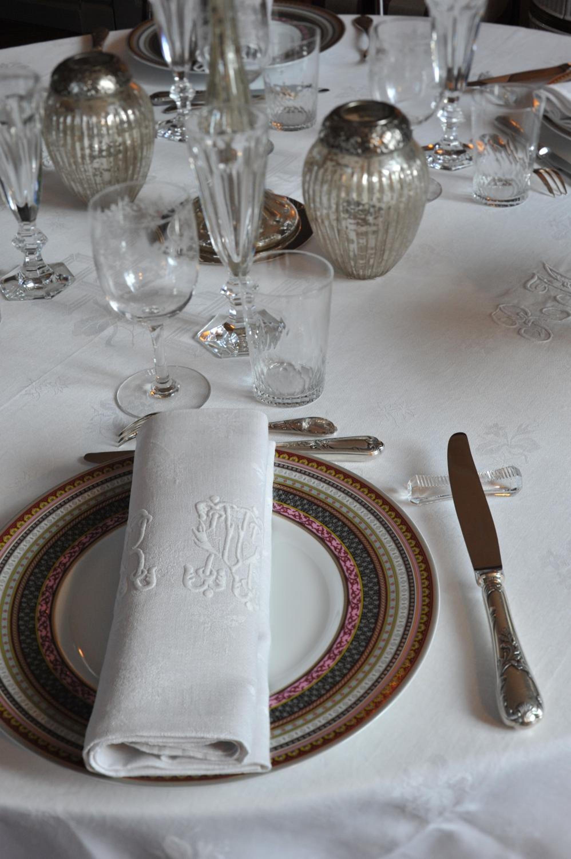 Una mesa dispuesta con un mantel doblado, un plato decorativo, un cuchillo y varias copas de vino.