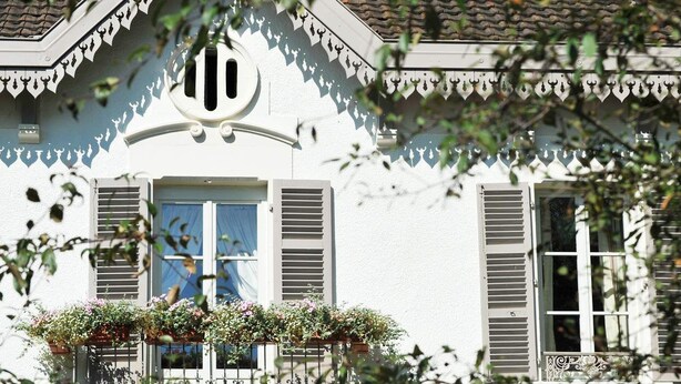 Un edificio blanco con balcón, contraventanas y una celosía decorativa.