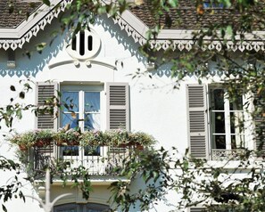 A white building with a balcony, shutters, and a decorative window grille.