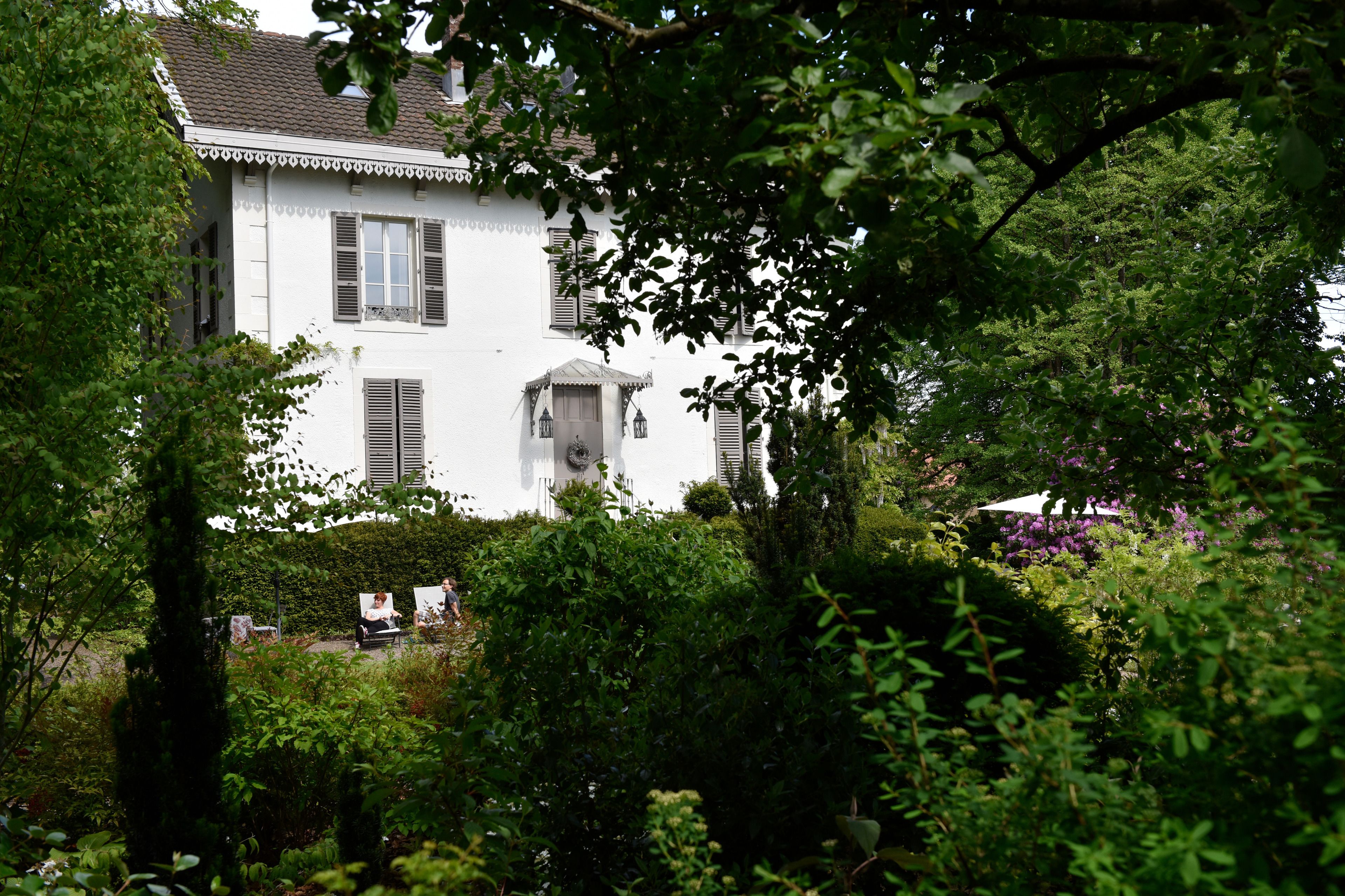 Ein weißes Haus mit Fensterläden, umgeben von üppigem Grün und einem Garten.