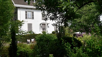Ein weißes Haus mit Fensterläden, umgeben von üppigem Grün und einem Garten.