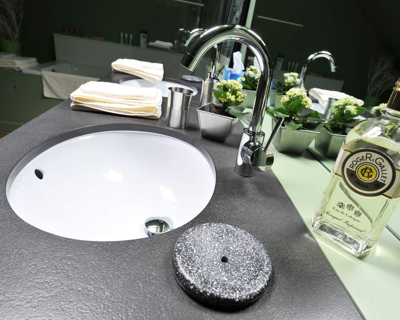 A bathroom sink with a modern faucet, a soap dish, a small container, and a bottle of Roger & Gallet cologne.