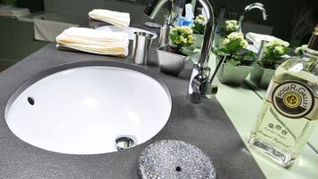 A bathroom sink with a modern faucet, a soap dish, a small container, and a bottle of Roger & Gallet cologne.
