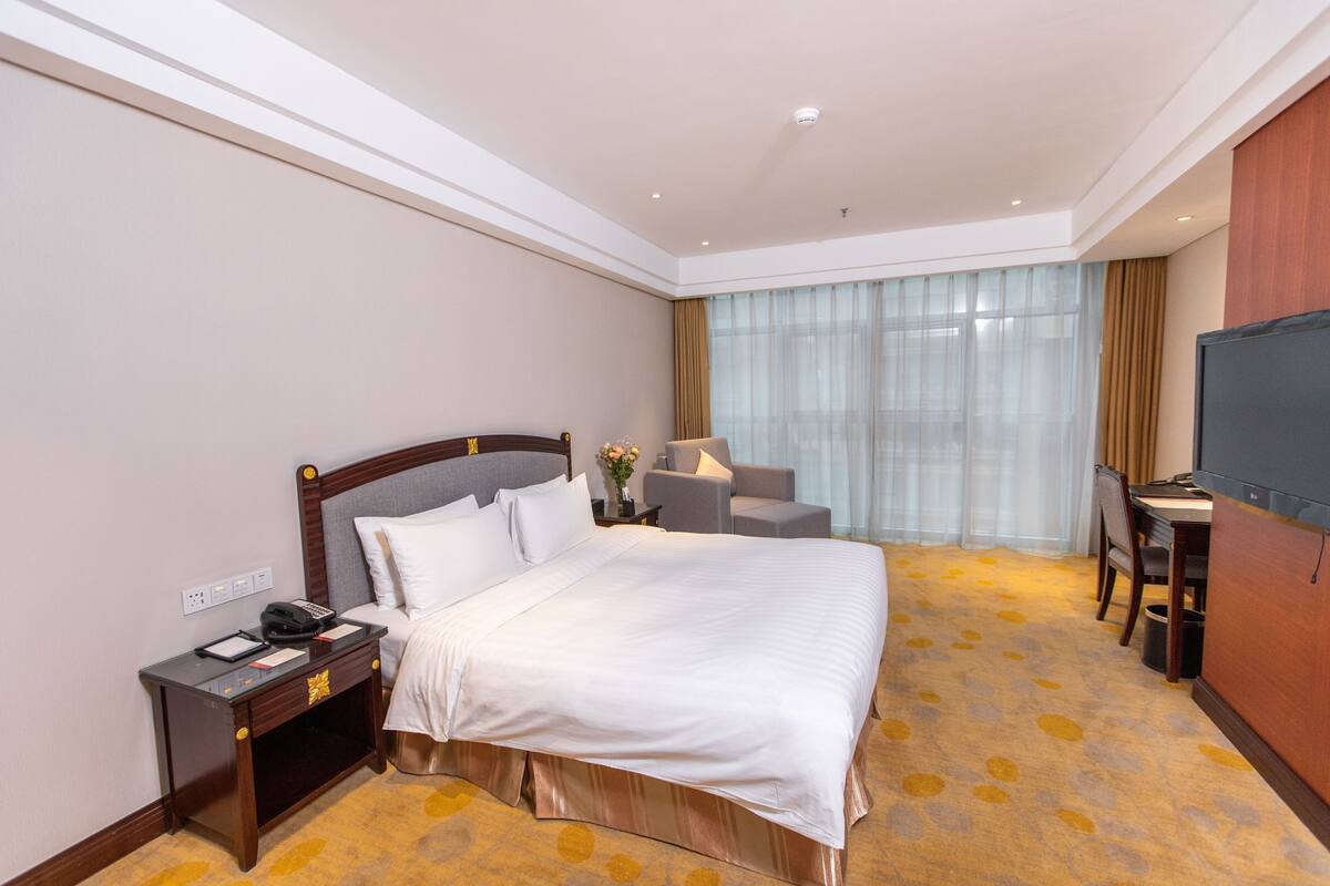 Une chambre d’hôtel avec un grand lit, une table de chevet, une lampe, un bureau et une télévision.