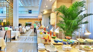 A spacious hotel lobby with a long buffet table, multiple dining tables, and a large potted plant. - Beijing Broadcasting Tower Hotel (Beijing)