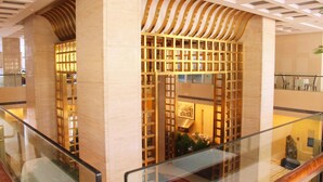 A hotel lobby with a modern design, featuring a glass railing, a central decorative wall with a geometric pattern, and a staircase leading to an upper level. - Beijing Broadcasting Tower Hotel (Beijing)