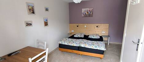 Un dormitorio con una cama de madera, una mesita y una silla. Hay cuadros en la pared y una lámpara en el techo.