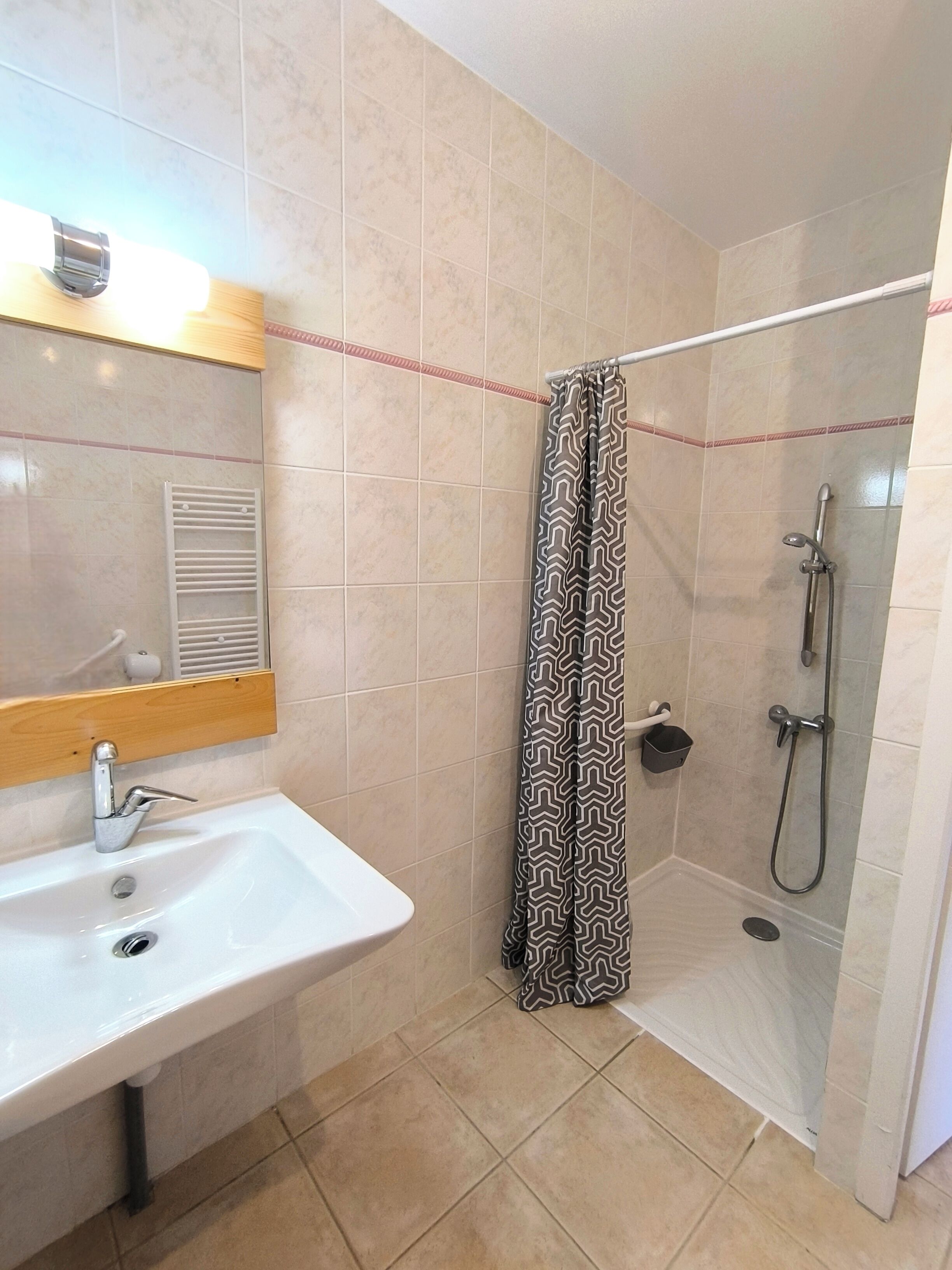 A bathroom with a sink, mirror, shower, and patterned shower curtain.