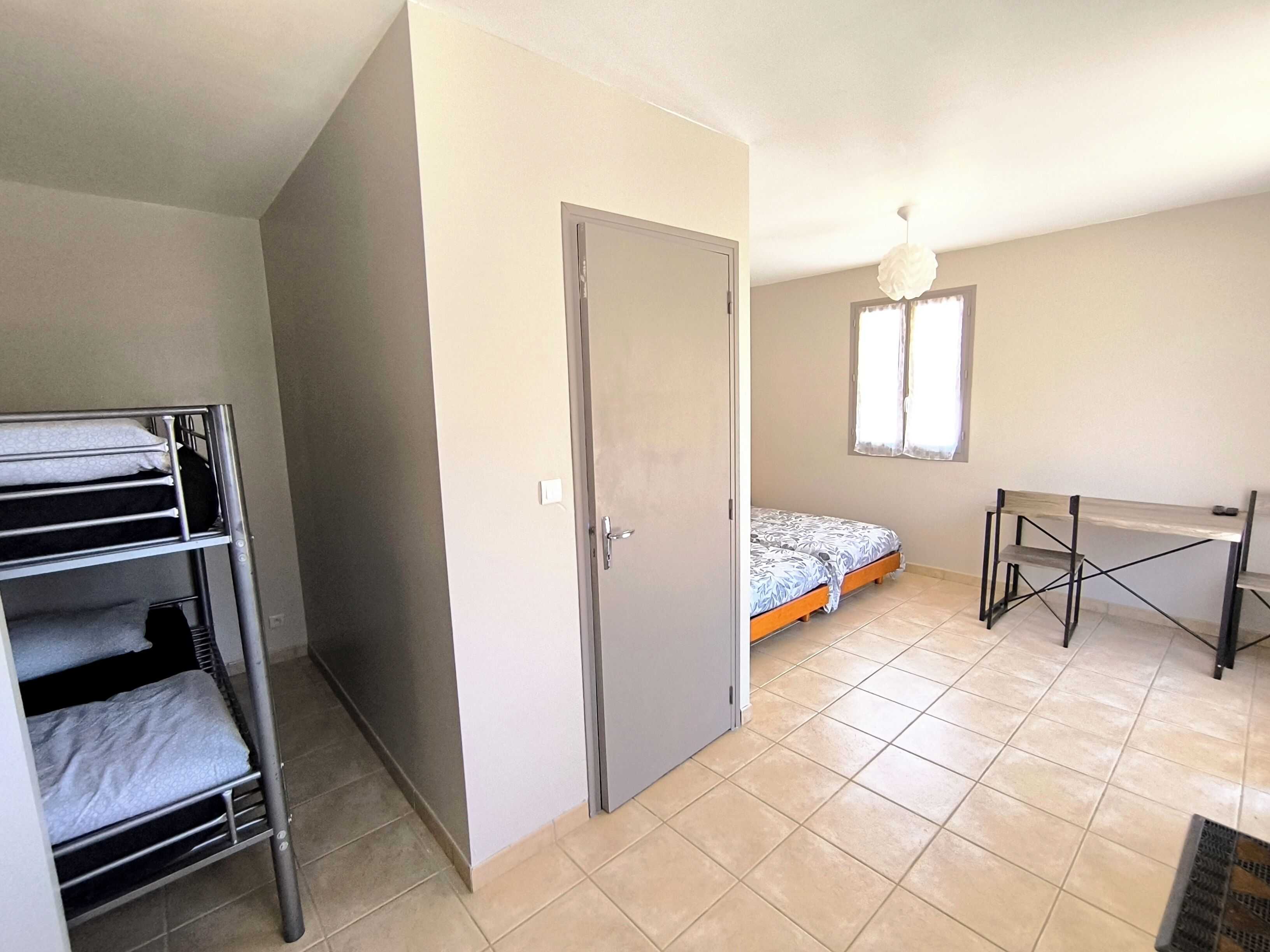 A bedroom with a bunk bed, a single bed, a desk, and a window.