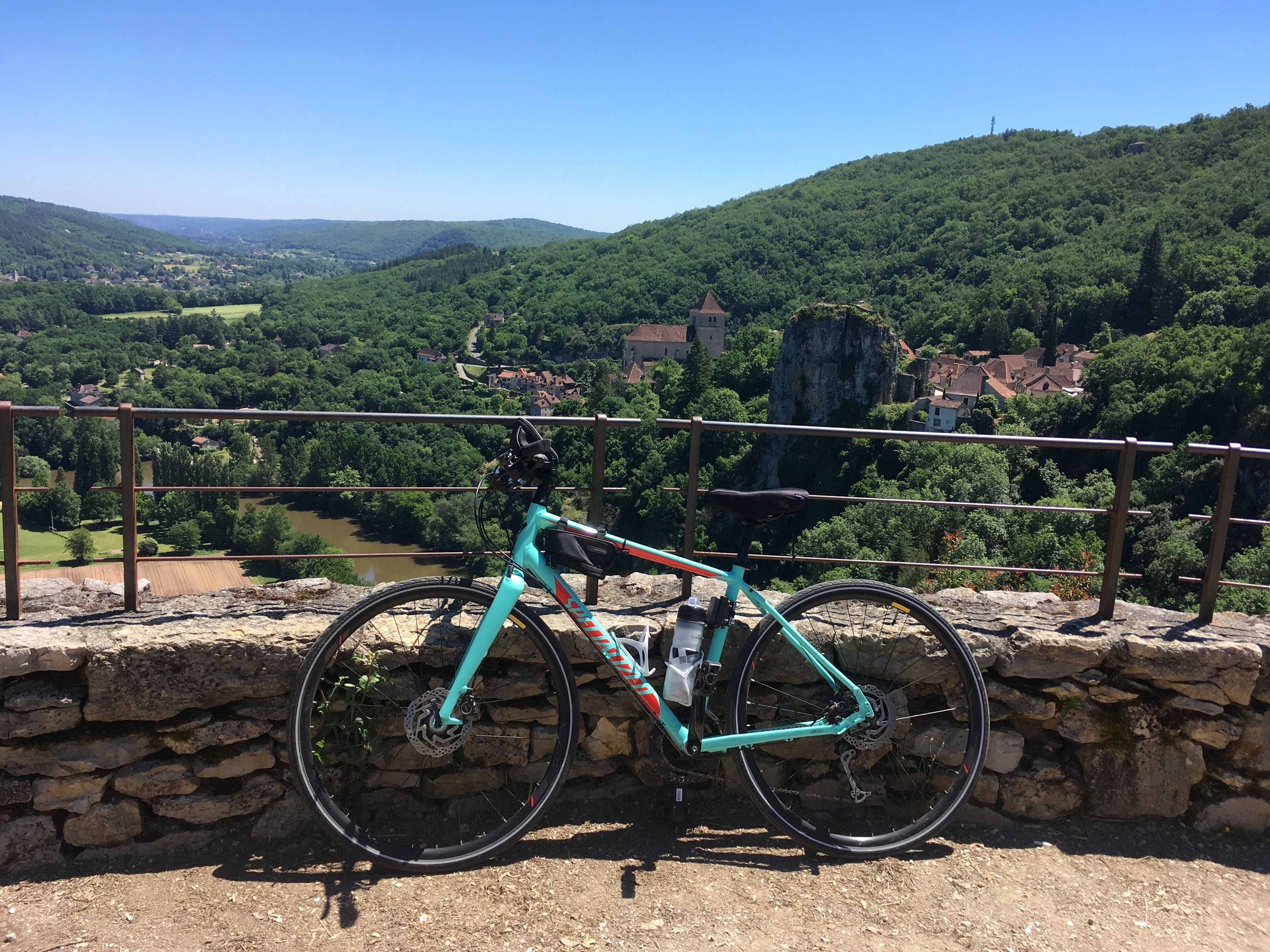 A bicycle parked on a stone wall overlooking a scenic landscape with a river, houses, and hills.