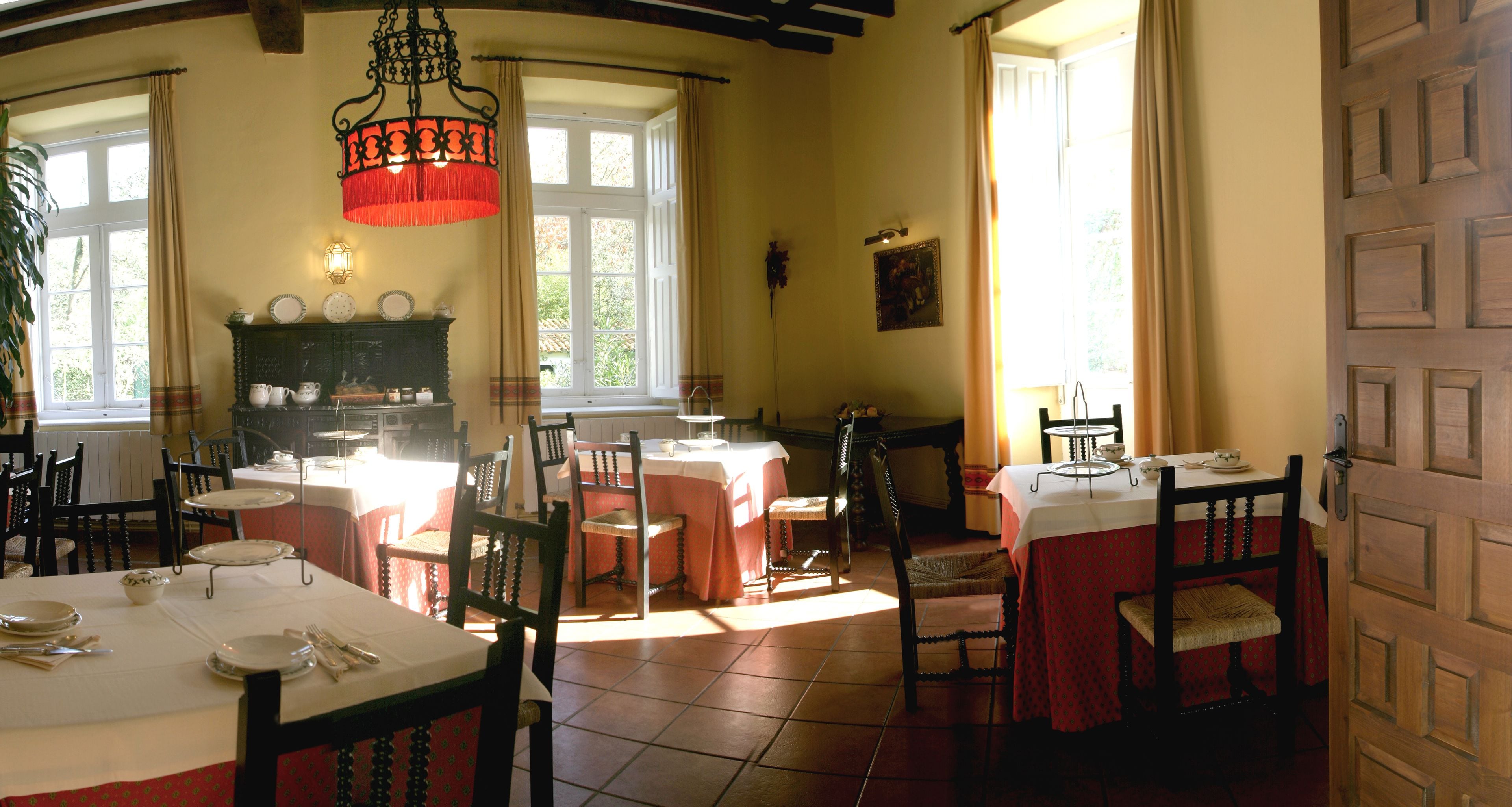 A dining area with multiple tables set for meals, a chandelier, and a view of the outdoors through large windows.