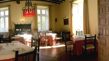 A dining area with multiple tables set for meals, a chandelier, and a view of the outdoors through large windows.