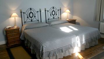 Una cama doble con cabecera metálica, dos mesitas de noche con lámparas, un aparador de madera y una colcha a cuadros.