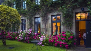 Un edificio con ventanas amplias, un jardín con flores rosadas y una pequeña mesa.