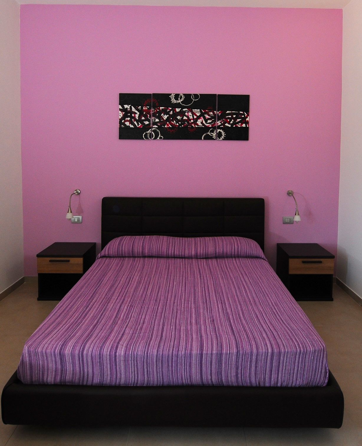A bedroom with a bed, two nightstands, and a wall-mounted artwork.