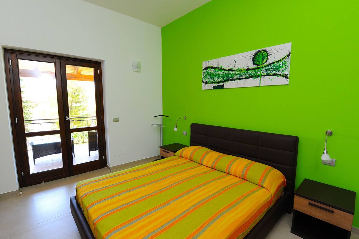 Ein Schlafzimmer mit einem Bett, einer grünen Wand, einem Fenster und einem Gemälde.