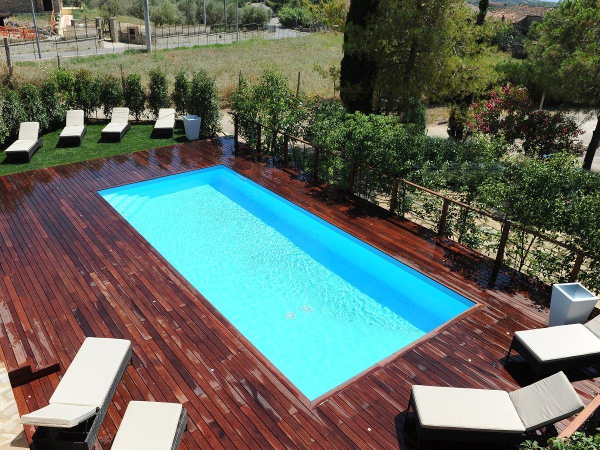 A rectangular swimming pool with a wooden deck surrounding it, equipped with several lounge chairs.
