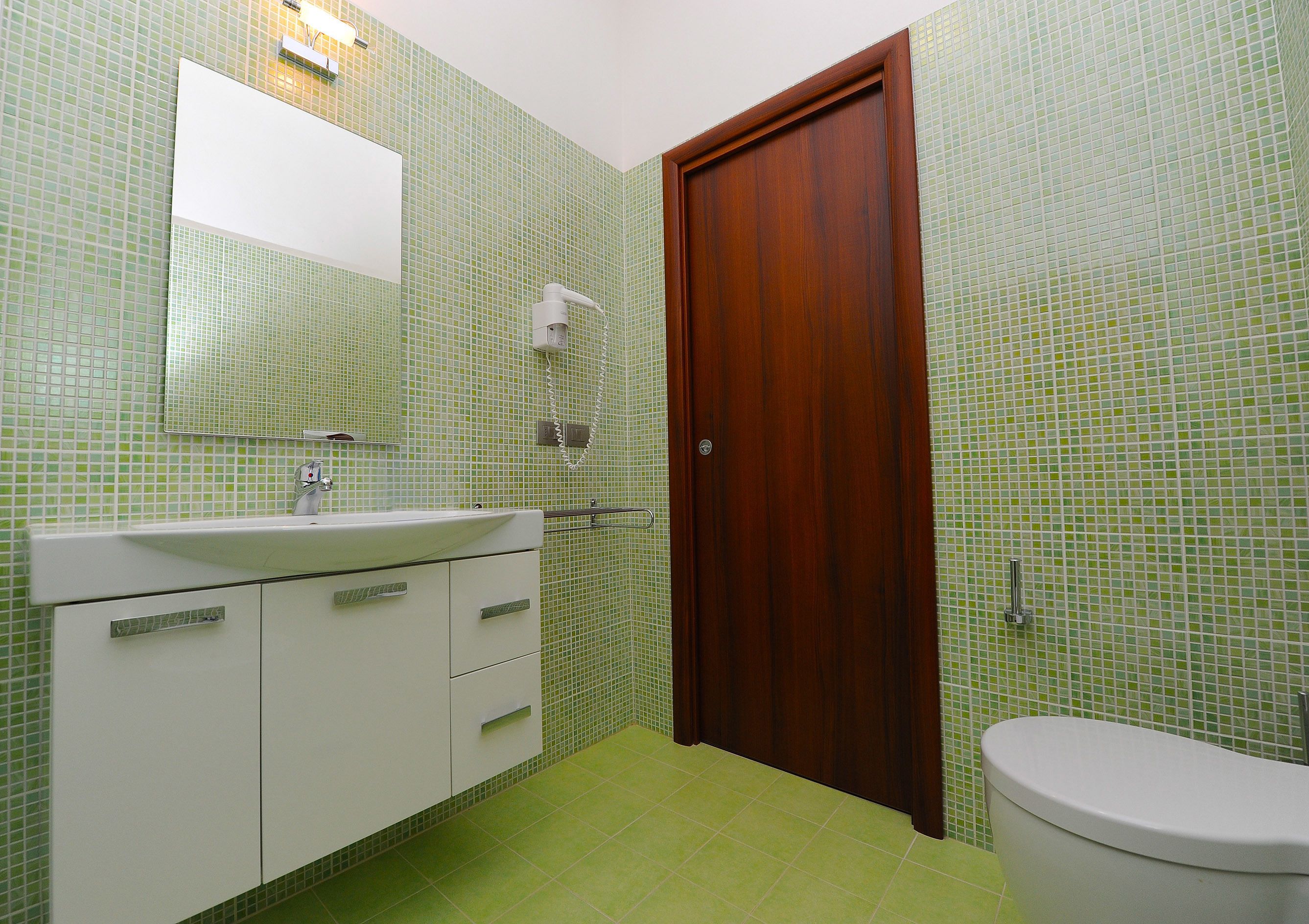 A bathroom with a green tiled wall, a wooden door, a white sink, and a toilet.