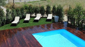 A swimming pool with wooden decking and white lounge chairs.