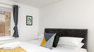 A hotel room with a bed, a window with curtains, a framed picture on the wall, and a yellow towel on the bed.