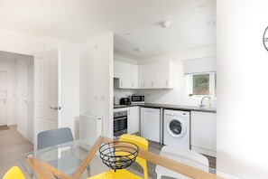 A modern kitchen with white cabinets, a microwave, oven, and washing machine.