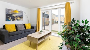 A modern living room with a sofa, coffee table, and a large window with yellow curtains.