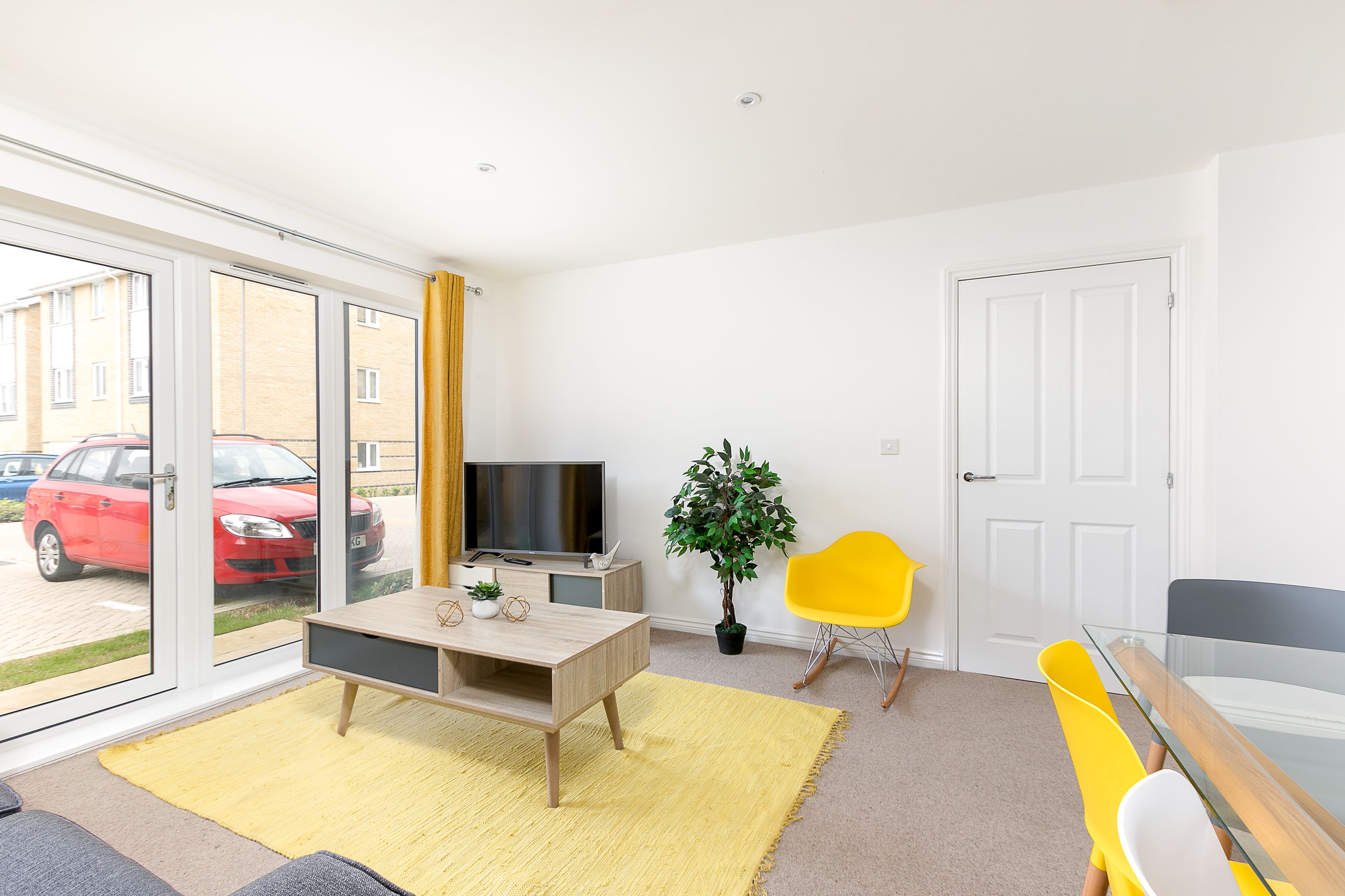 A modern living room with a TV, a yellow chair, a wooden table, and a potted plant.