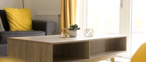 A modern living room with a wooden coffee table, a potted plant, and decorative items.