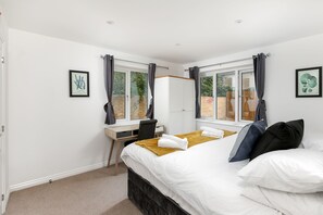 A bedroom with a bed, a desk, and two windows with curtains. - Hertford Serviced Apartments  (Hertford)