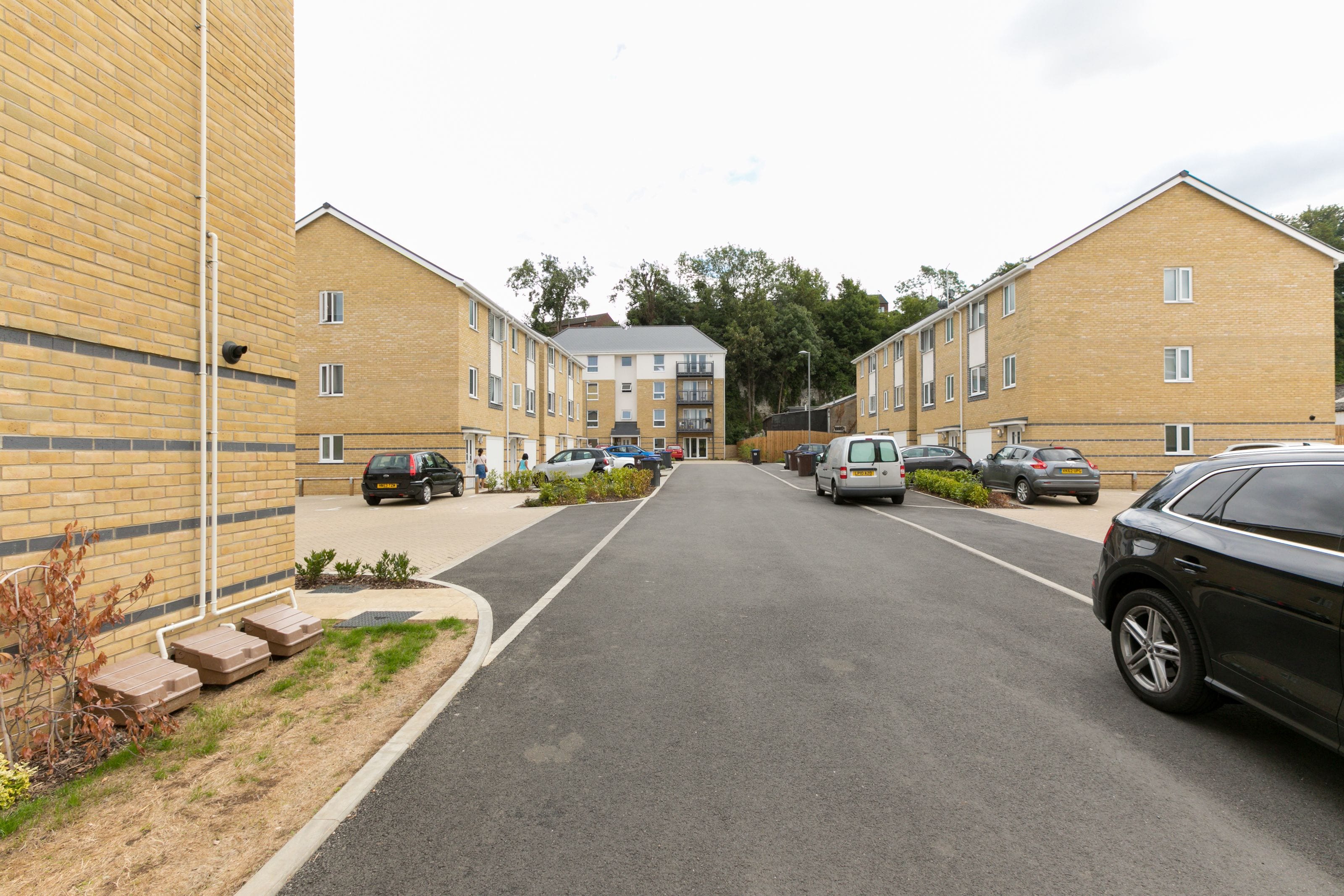 A street view of a residential area with brick buildings, parked cars, and a clear sky.
