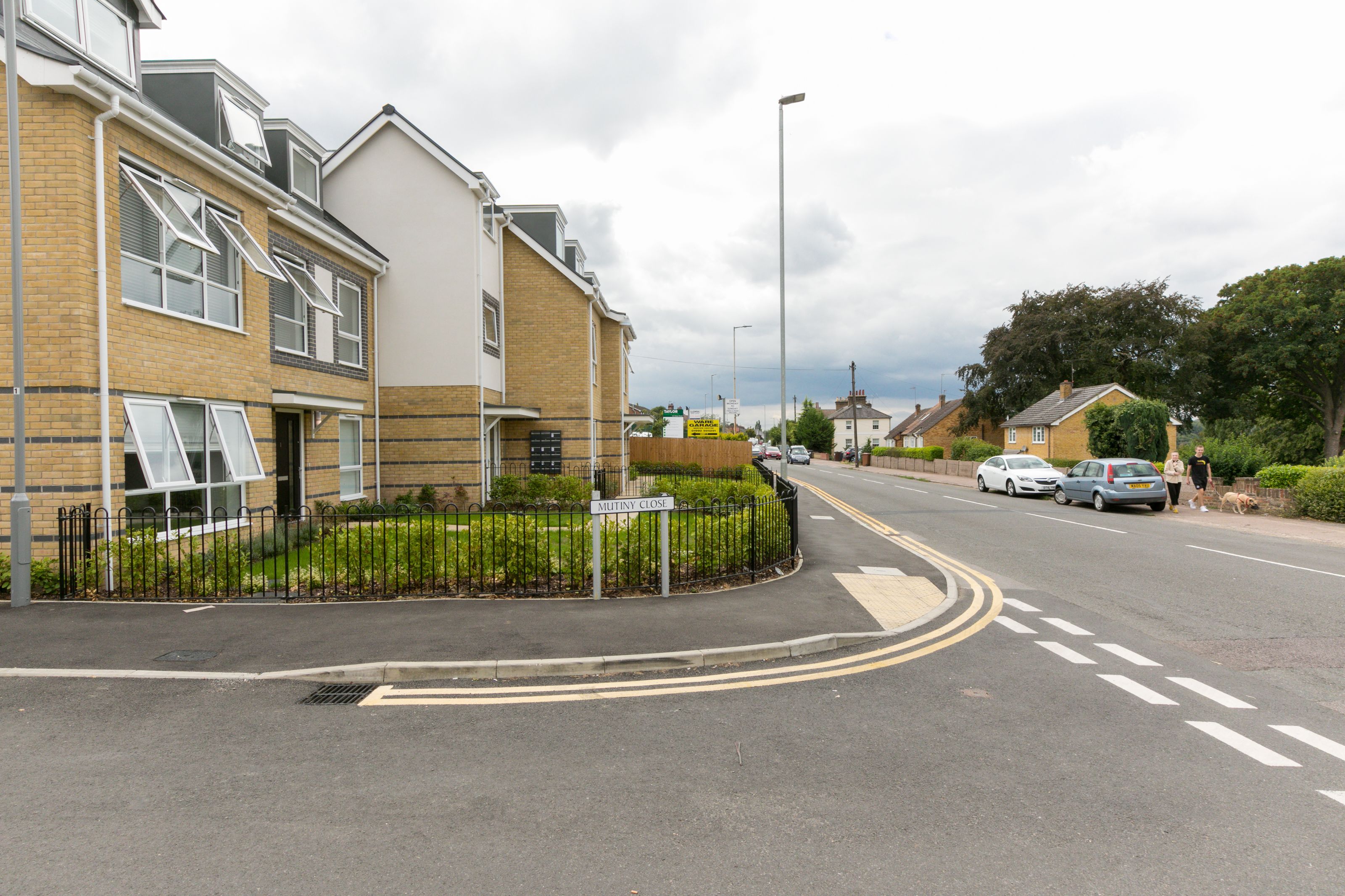 A residential street with houses, a 'MUTINY CLOSE' sign, and cars parked along the road.