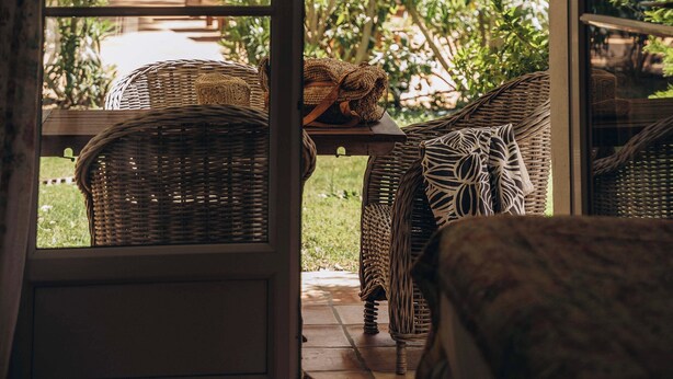 A room with wicker furniture and a view of a garden through a glass door. - La Villa d'Andrea (Ramatuelle)