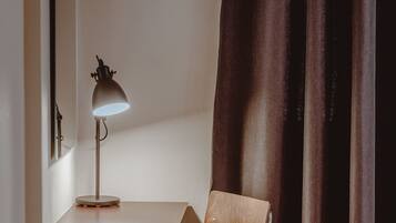 Une pièce d’angle avec un bureau en bois, une chaise, une lampe et une fenêtre avec des rideaux.