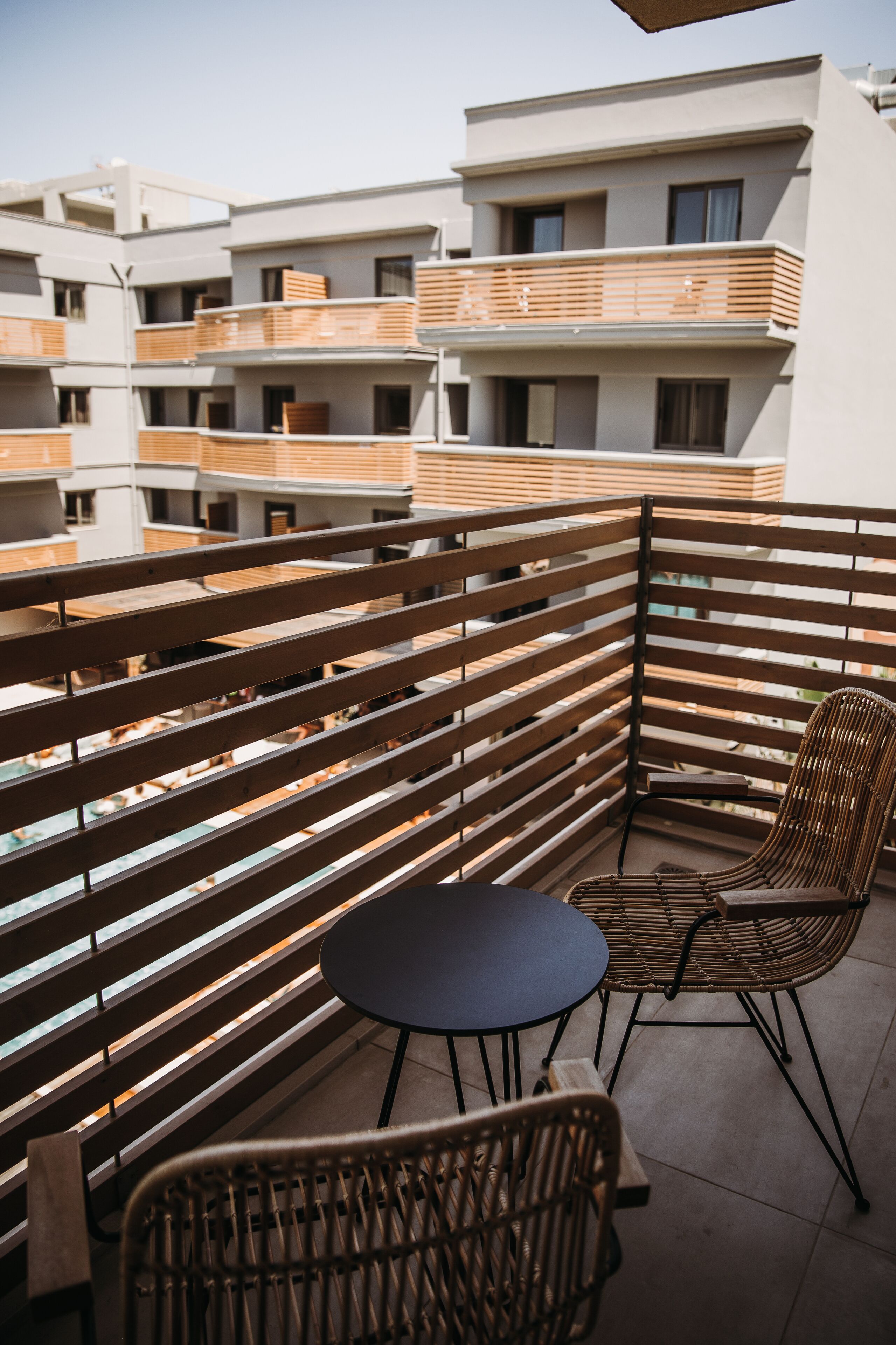Un balcone con persiane in legno, un tavolo rotondo e due sedie in vimini.