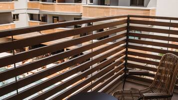 Un balcone con persiane in legno, un tavolo rotondo e due sedie in vimini.