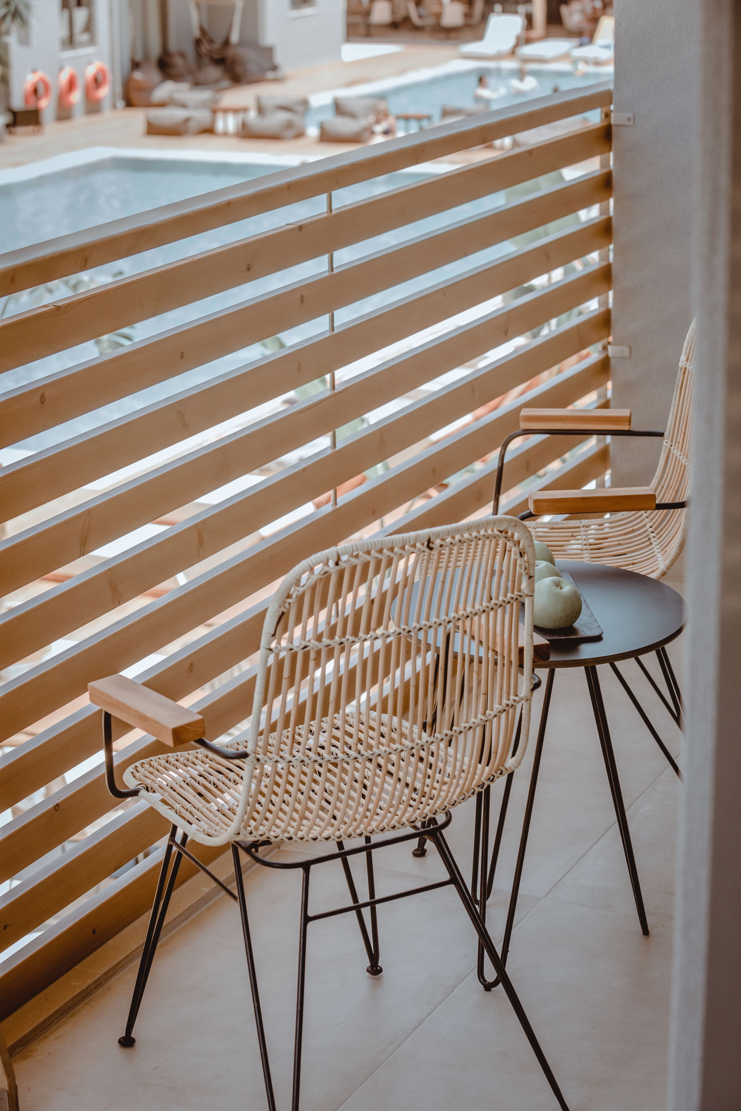 A balcony with two wicker chairs and a small table, overlooking a swimming pool area.