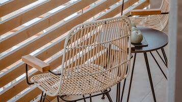 A balcony with two wicker chairs and a small table, overlooking a swimming pool area.