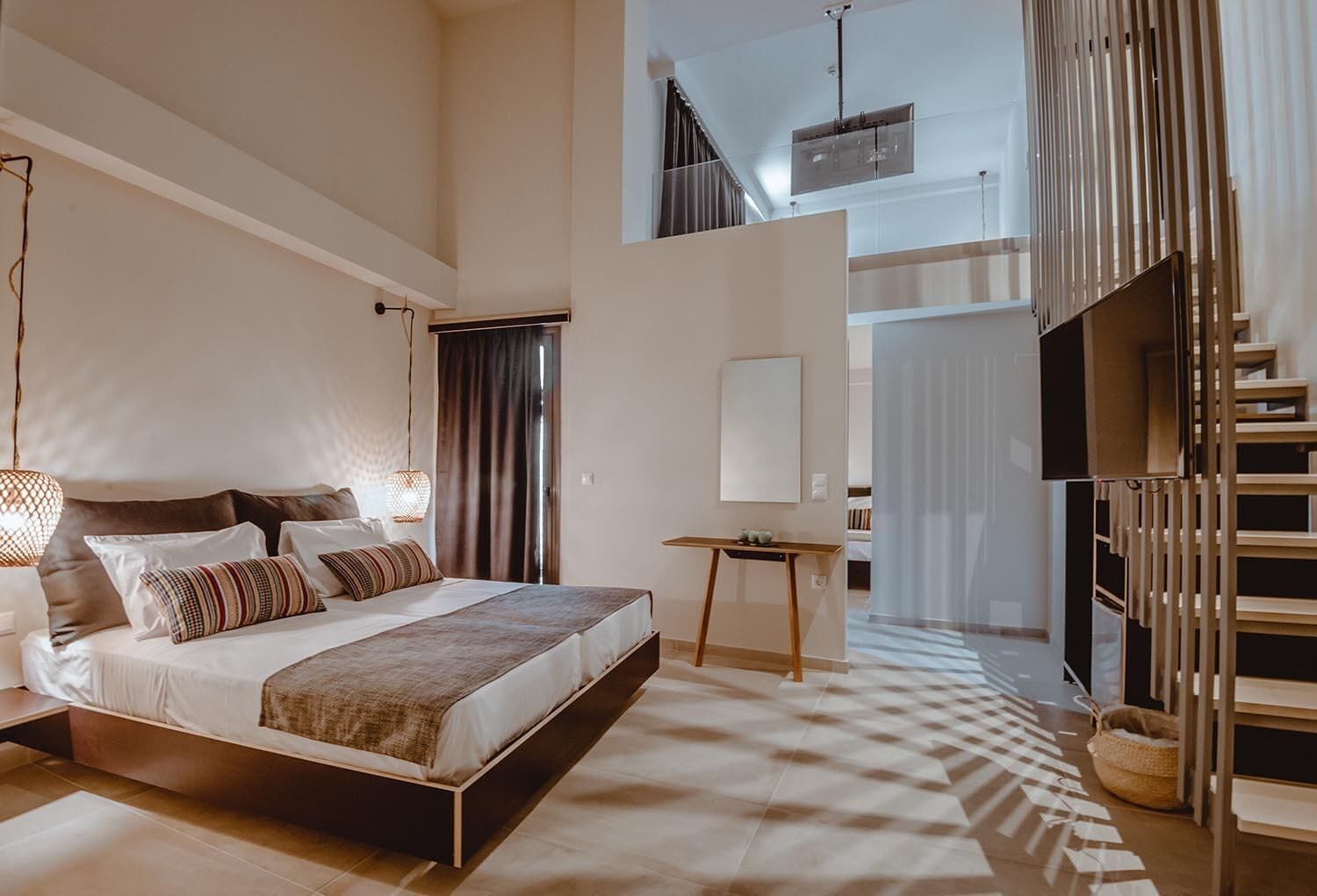 A modern bedroom with a large bed, a small table, and a staircase leading to an upper level.