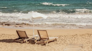 A beach with two wooden lounge chairs and a white umbrella, positioned on the sand facing the ocean. - Cook's Club Hersonissos Crete (Hersonissos)