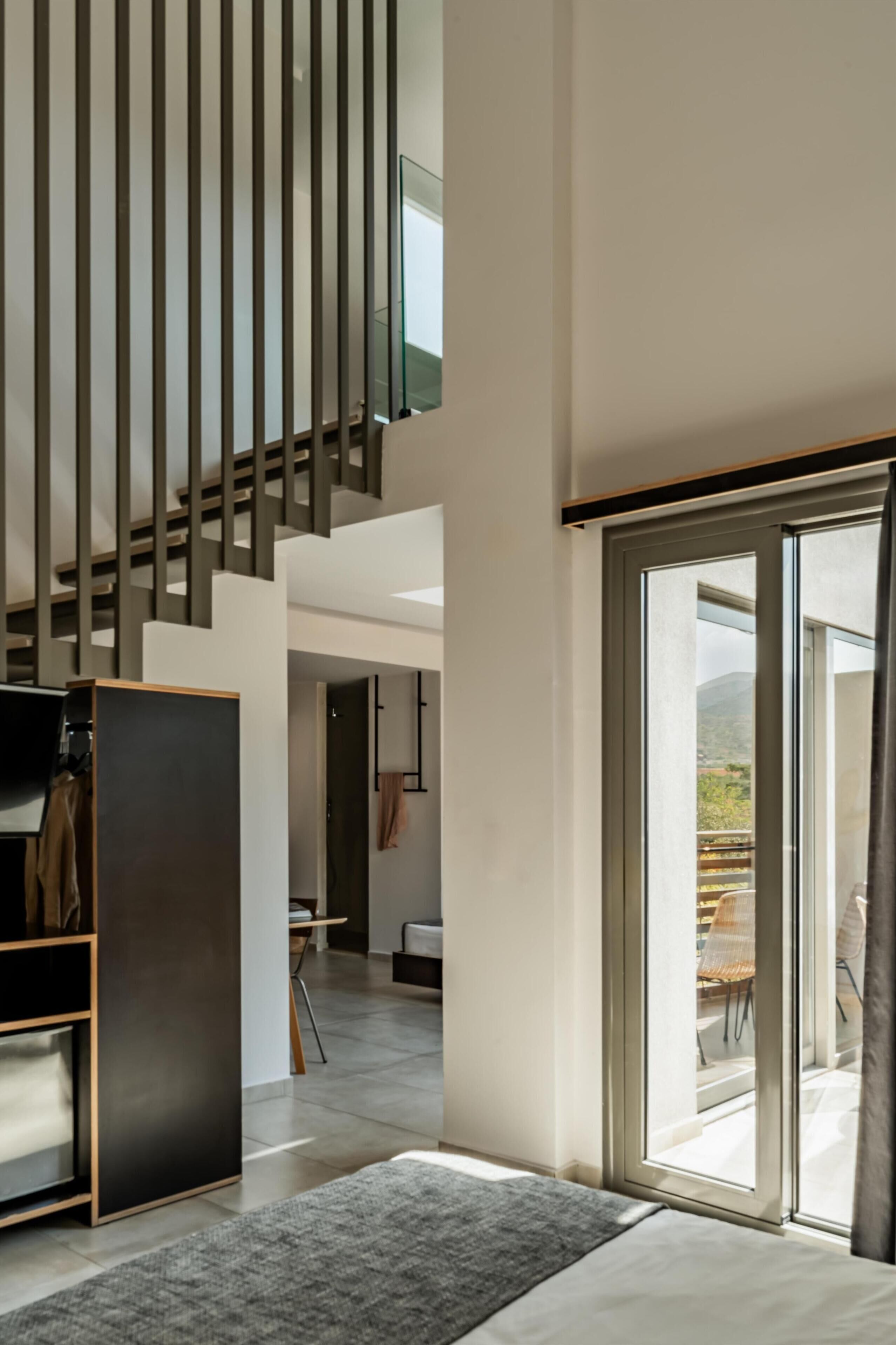 Un intérieur moderne avec un escalier, une porte-fenêtre coulissante donnant sur un balcon et un lit.