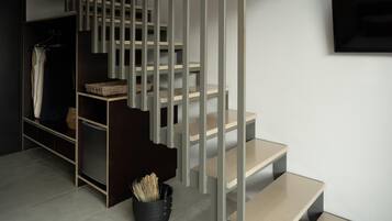 A modern staircase with a minimalist design, a flat-screen TV mounted on the wall, and a basket of items on the floor.
