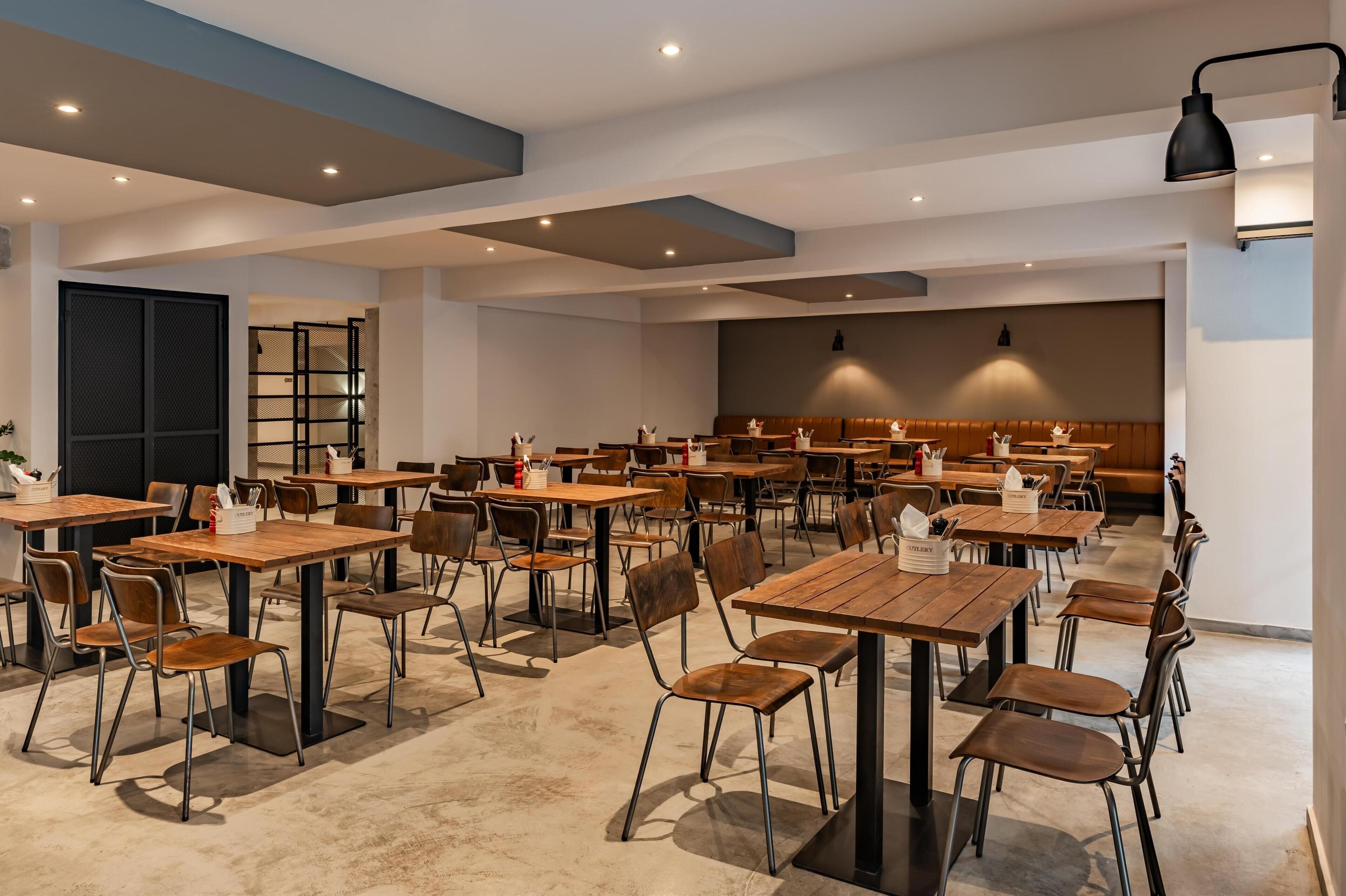 Un comedor amplio con varias mesas y sillas de madera, un área de estar central con un banco, y un diseño de techo moderno.