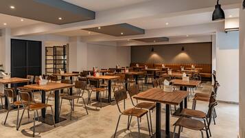 Un comedor amplio con varias mesas y sillas de madera, un área de estar central con un banco, y un diseño de techo moderno.