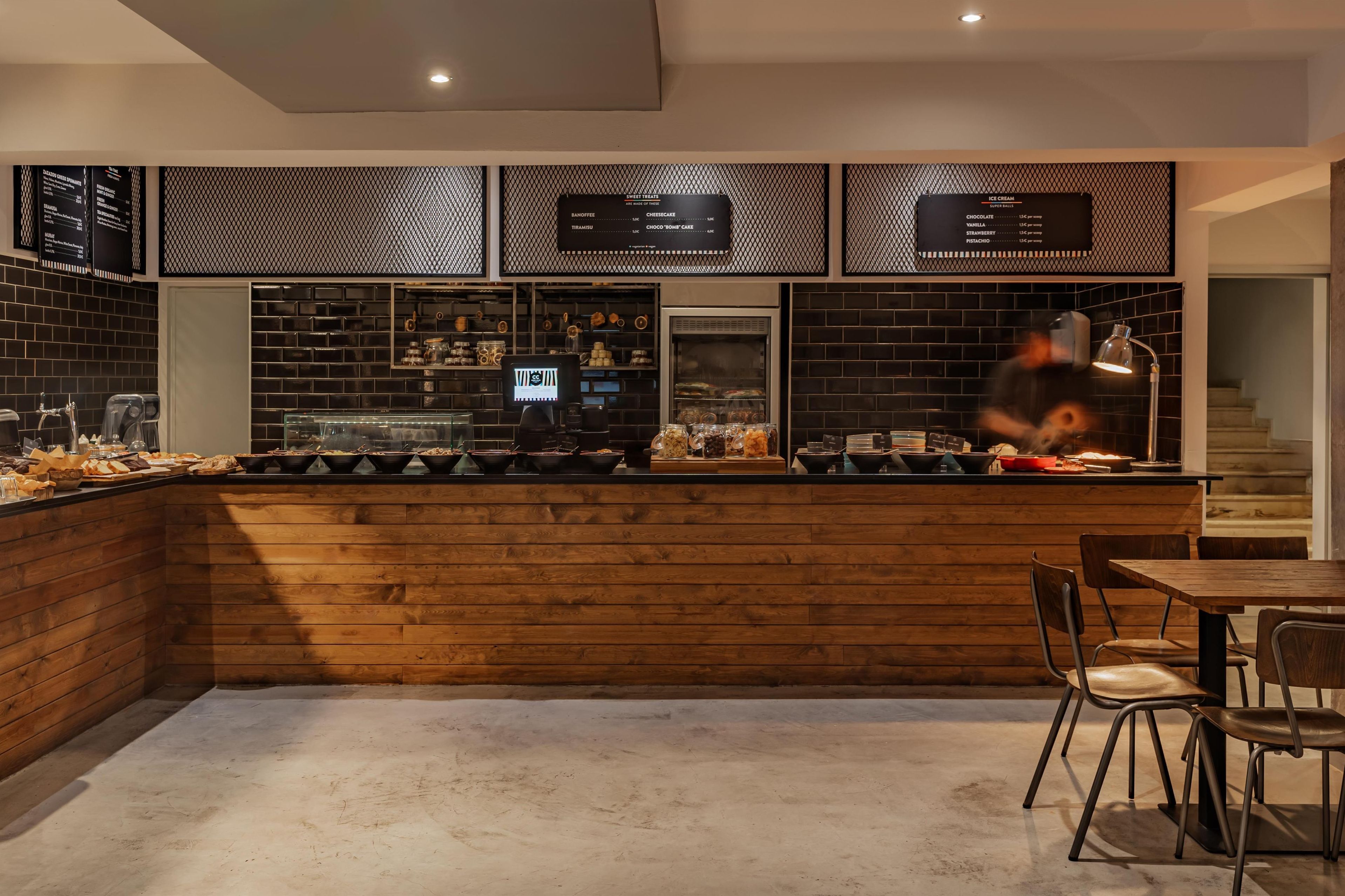 A modern bar area with a wooden counter, seating, and menu boards.