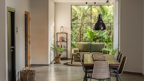 A modern living room with a large window, a sofa, a dining table, and a bookshelf. - Cook's Club Hersonissos Crete (Hersonissos)
