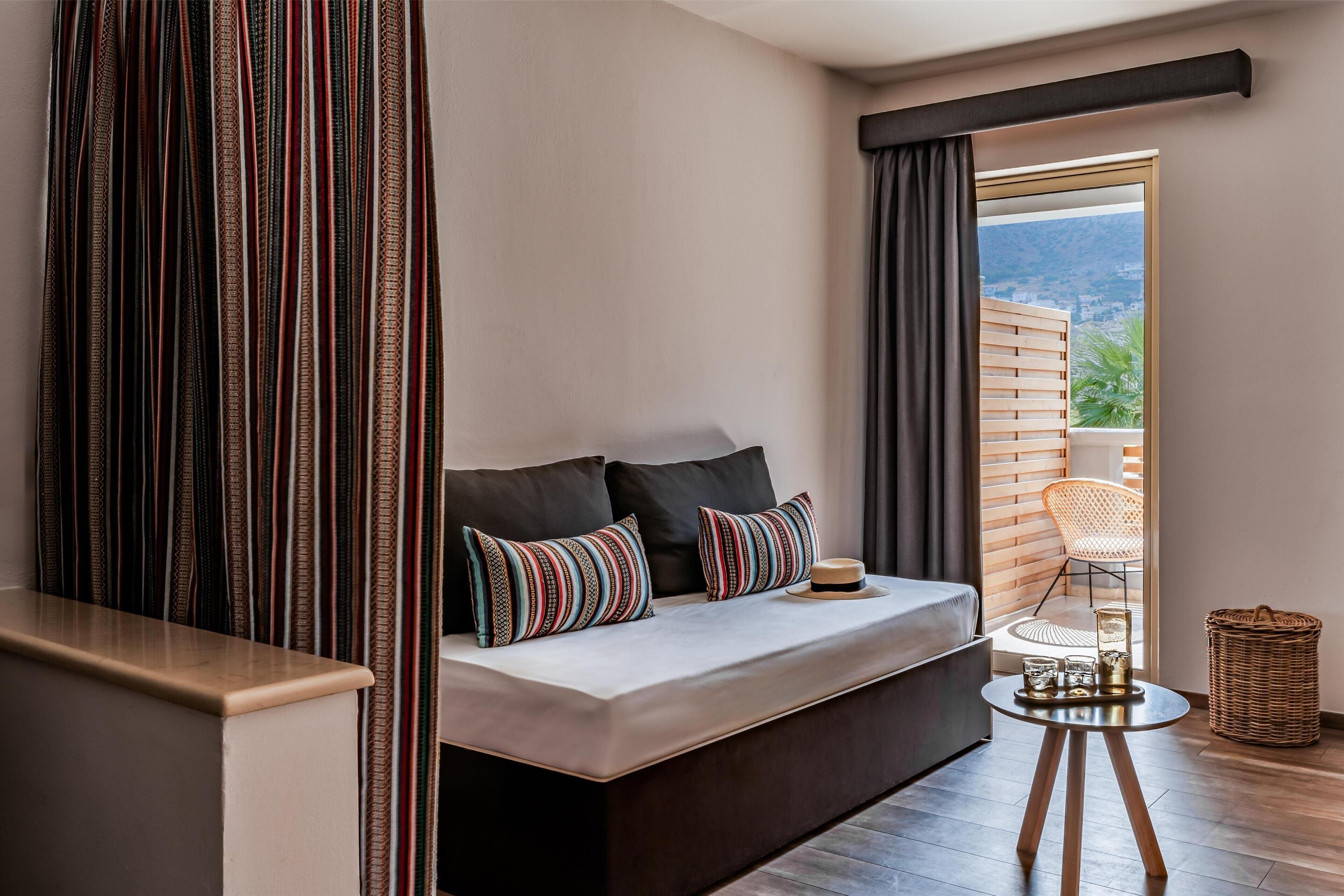 A modern bedroom with a sofa bed, striped curtains, a small round table with glasses, and a wicker basket.