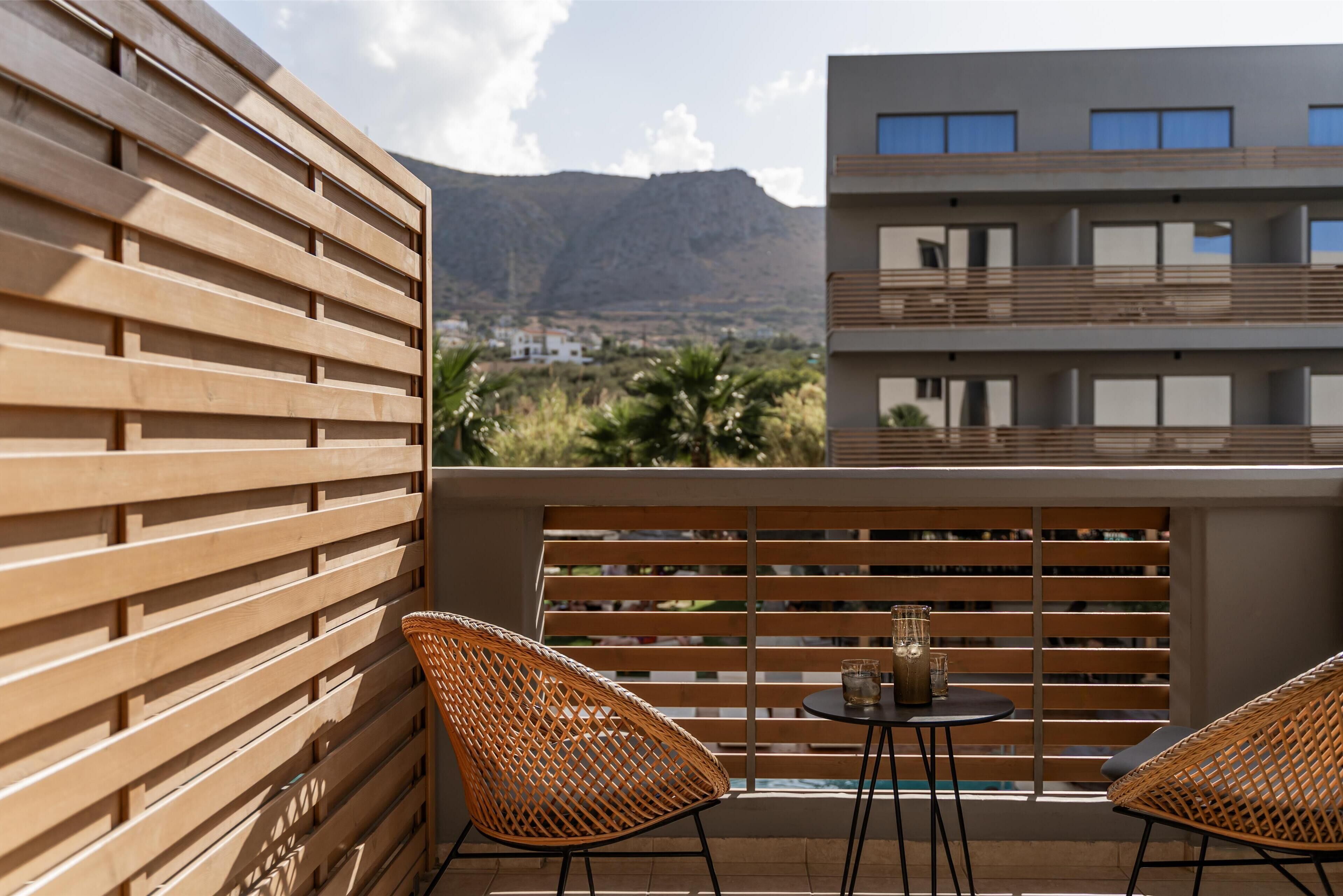 A balcony with wooden slats, wicker chairs, and a small table with a glass.