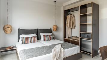 A modern bedroom with a large bed, a wardrobe, and a small table with a cup and sunglasses.