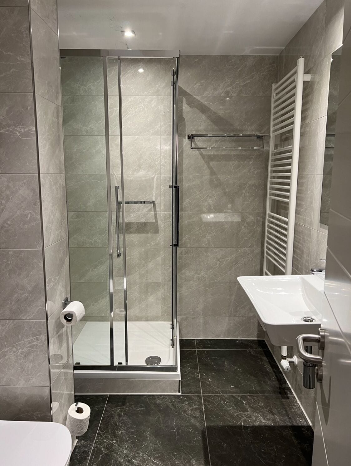 A modern bathroom with a glass-enclosed shower, a white sink, and a towel rack.
