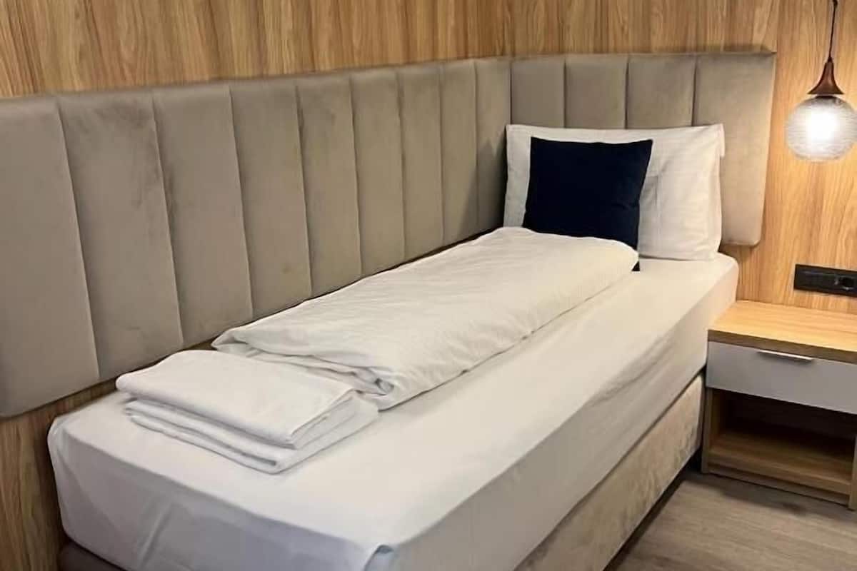 Un dormitorio moderno con un panel de madera en la pared, un cabecero acolchado, una mesita de noche con lámpara y una cama bien hecha.